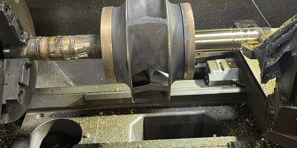 Close-up of a machined pump rotor in a lathe during a custom rebuild process, showing both worn and freshly turned metal sections.