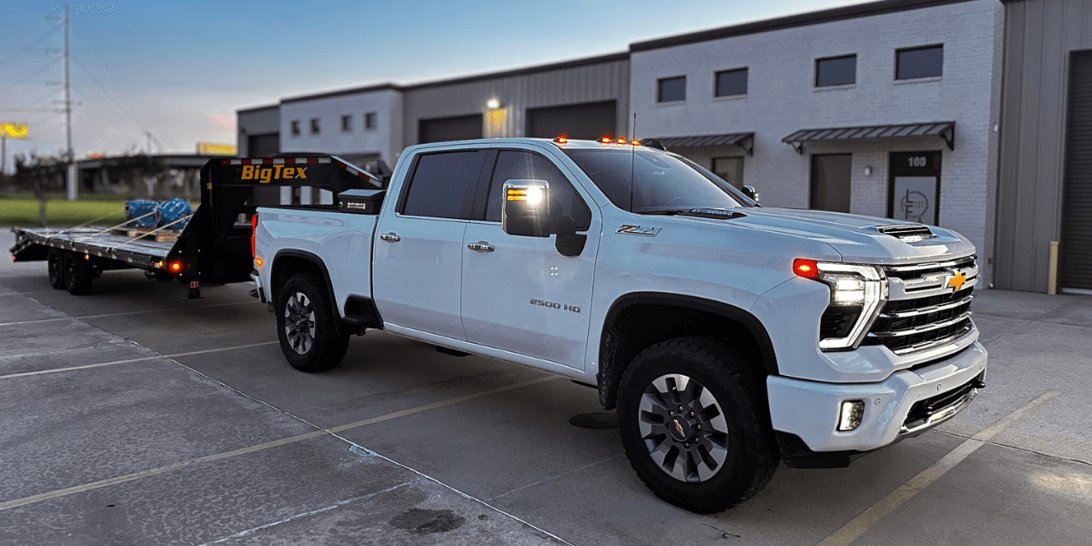 White Chevrolet 2500 HD service truck hitched to a Big Tex flatbed trailer, loaded with equipment, parked in front of EV Pump’s facility—highlighting mobile delivery and on-site service capabilities.