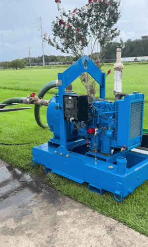 Rebuilt Tier 3 trash pump skid painted blue on a steel frame with forklift pockets. Features discharge piping with butterfly and ball valves, green suction hose, and a diesel engine with control panel. Photographed on concrete in Lafayette, LA.