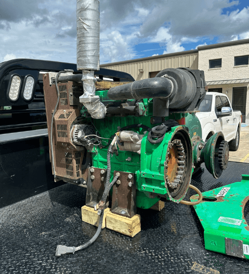 Close-up of a green diesel engine on a flatbed, showing the exhaust system, air intake, and flywheel housing — part of a pump skid assembly being serviced.