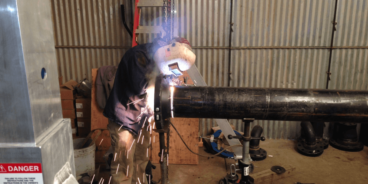 Welder at work welding flange to pipe on infrastructure project